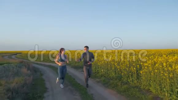 体育活动快乐的运动员戴着卡尼卡隆辫子的男女在油菜花草地上在大自然中奔跑视频的预览图
