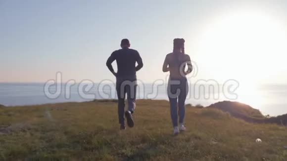 心脏锻炼运动男性和女性戴着卡尼卡隆的辫子在明亮的天空下在河边奔跑视频的预览图