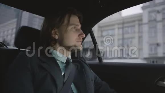 穿着开心果衬衫和灰色西装的棕色头发的人坐在车上系安全带四处张望视频的预览图