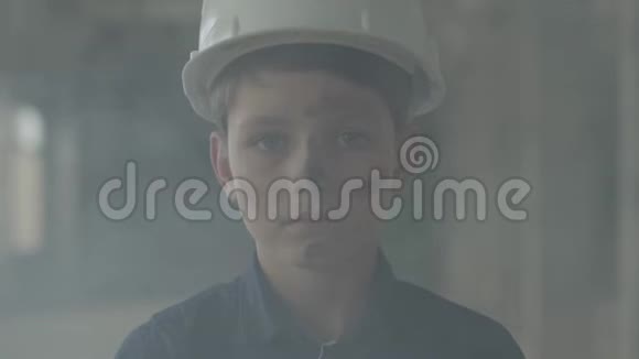 肖像可爱的男孩戴着保护头盔看着镜头背景的室内烟雾火灾概念视频的预览图