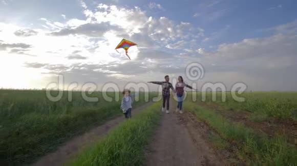 快乐的小男孩手里拿着风筝在活跃的周末在农村慢动作地跑在年轻父母身边视频的预览图
