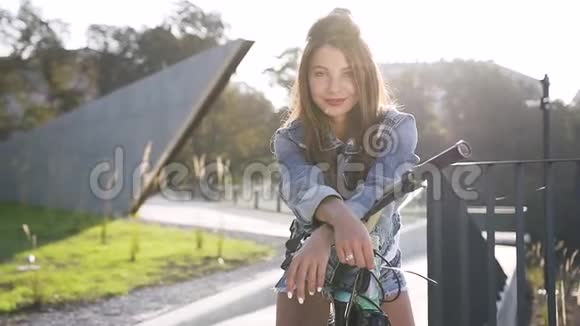 可爱快乐的年轻女子的迷人肖像她留着长发骑着自行车穿着牛仔裤在镜头上摆姿势视频的预览图