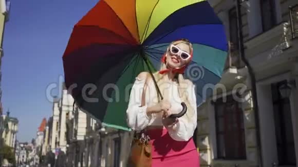 漂亮的年轻女人看着相机拿着五颜六色的雨伞站在街上时尚迷人视频的预览图