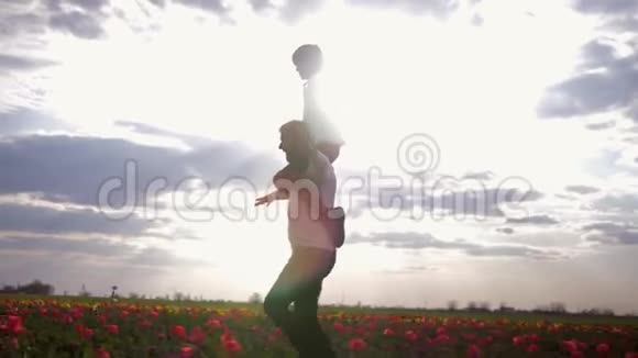 父子关系快乐的爸爸和儿子张开双臂坐在一边在鲜花草地上玩得开心视频的预览图
