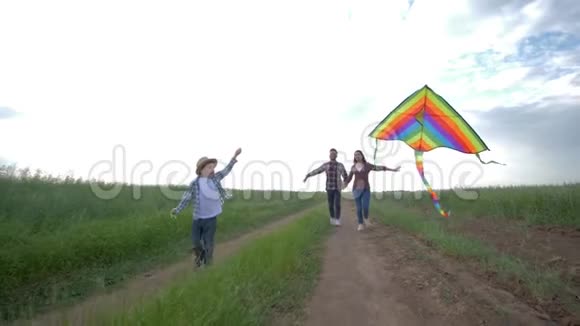 周末带着风筝的孩子在阳光明媚的天空中慢悠悠地跑在农村的年轻父母身边视频的预览图