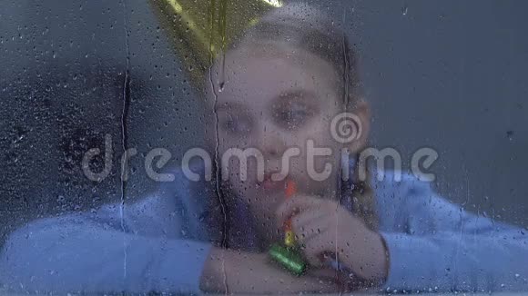 悲伤孤独的女孩带着派对鼓风机在雨中看着窗户没有朋友视频的预览图