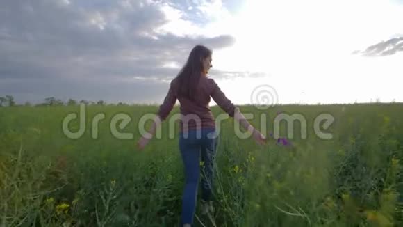 少女漫步绿油油的油菜花田在天空的背景下欣赏大自然的美景视频的预览图