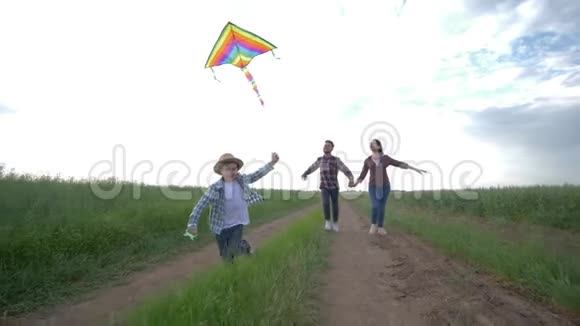 一家人无所事事手里拿着风筝的小男孩在年轻父母的背景下缓慢地在农村奔跑视频的预览图
