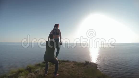 海上冥想日落时分男人和女人在山上用美丽的姿势做瑜伽练习视频的预览图