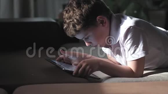 穿白色t恤的男孩短发躺着平板电脑站在监视器上视频的预览图