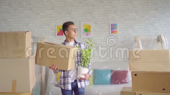 一个带着一朵花和一个盒子的积极的年轻人搬到了一间新公寓视频的预览图