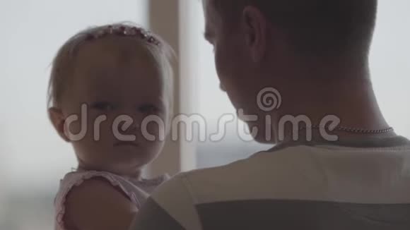 英俊的年轻人把小女孩抱在怀里在窗前特写作为父亲的乐趣爱视频的预览图