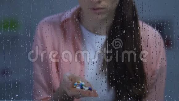 悲伤孤独的不健康的女人捧着药掌坐在雨窗附近视频的预览图