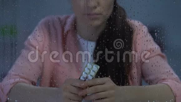 抑郁孤独的女性在雨窗附近拿着一包水泡药丸疾病视频的预览图