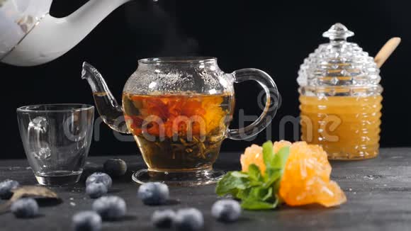 在玻璃茶壶里倒开水绿色的中国花茶绽放红花茶的漂浮蓝莓视频的预览图