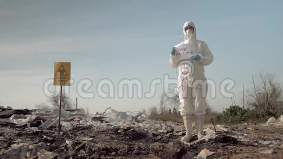 环保主义穿着防护服装的妇女戴着面具在垃圾填埋场张贴有防止污染标语的海报视频的预览图