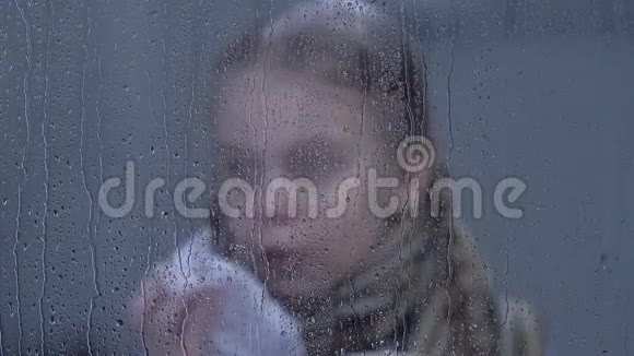 可爱的小女孩打喷嚏透过雨窗看镜头流感视频的预览图