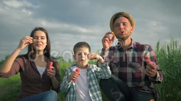 美丽的年轻家庭缓慢地吹着许多泡泡父母带着穿格子衬衫的儿子在户外玩得很开心视频的预览图