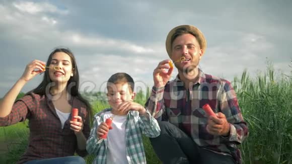 年轻家庭在户外玩肥皂泡的肖像孩子和爸爸妈妈穿着格子衬衫玩得开心视频的预览图