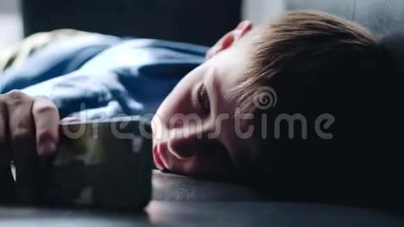 男孩躺在沙发上用智能手机看着悲伤的眼睛幼儿情绪眼睛视频的预览图