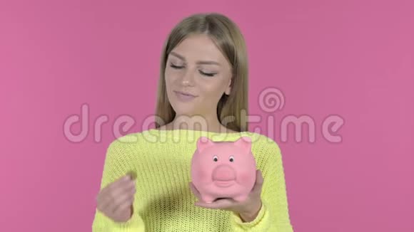 野心勃勃的少女在储蓄罐里插入硬币粉红色背景视频的预览图