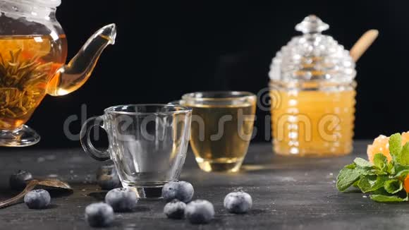 茶被缓慢地倒入玻璃透明茶杯中一杯茶和茶壶绿色中国花茶绽放视频的预览图