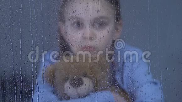 青春期前被遗弃的女孩拥抱泰迪熊在雨天看着窗户视频的预览图