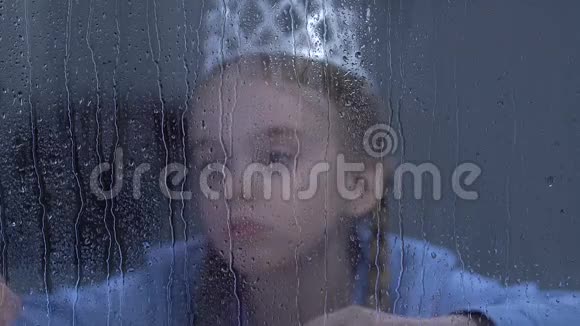 带着魔杖的女孩戴着公主王冠在雨窗后孤独地度过视频的预览图