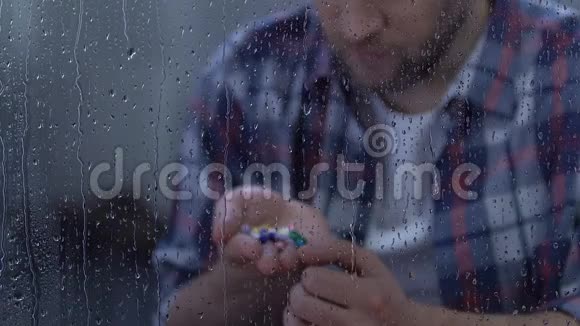沮丧的病人捧着满满一掌的药物坐在雨窗后视频的预览图