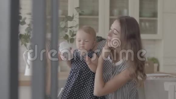 美丽微笑的年轻女子向她的女婴展示如何从厨房的婴儿瓶中喝酒幸福的概念视频的预览图