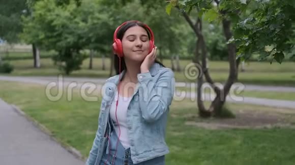 有趣的快乐女孩在公园附近的树上跳舞听着耳机上的音乐心情愉快特写视频的预览图