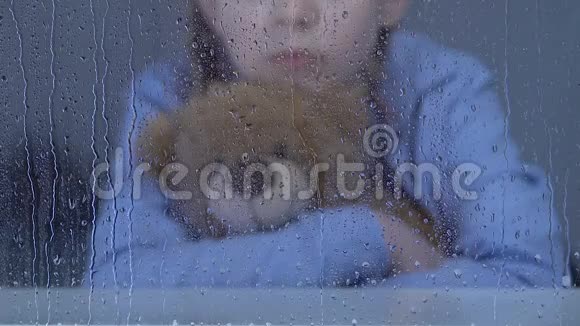 小女孤儿坐在雨窗后抱着玩具熊做梦视频的预览图