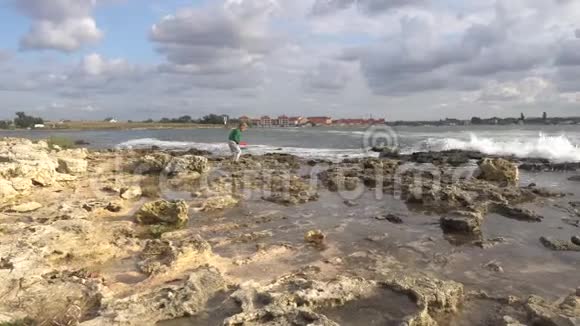 孩子走在海礁上试图坐在石头上视频的预览图