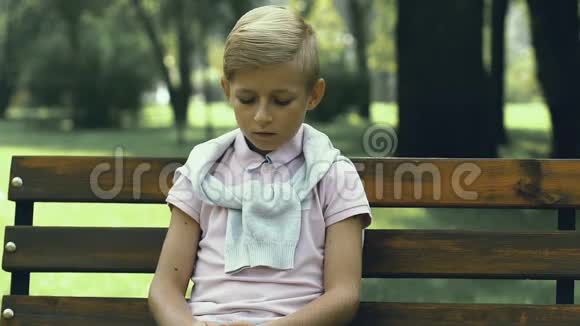 不快乐的小男孩独自坐在公园的长凳上校园欺凌和残忍视频的预览图