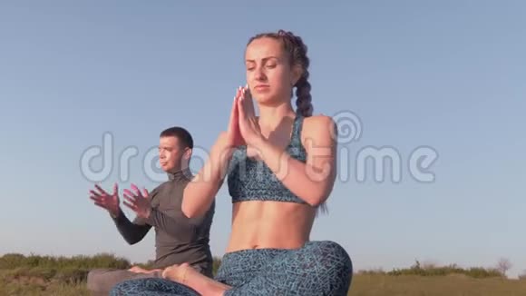 瑜伽的生活方式瑜伽的女人和男人在莲花的位置冥想与大自然和谐地坐在草地上对抗天空视频的预览图
