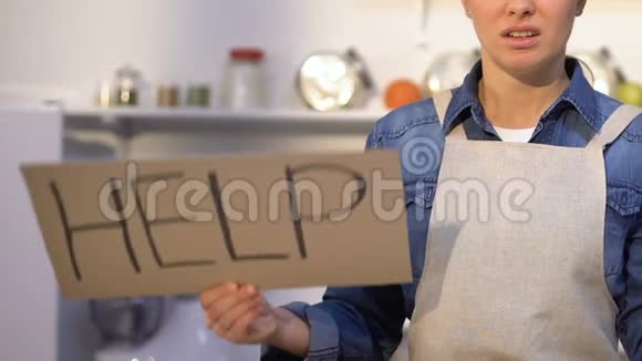 穿着围裙的女人站在厨房里拿着帮助标志开始做饭了视频的预览图