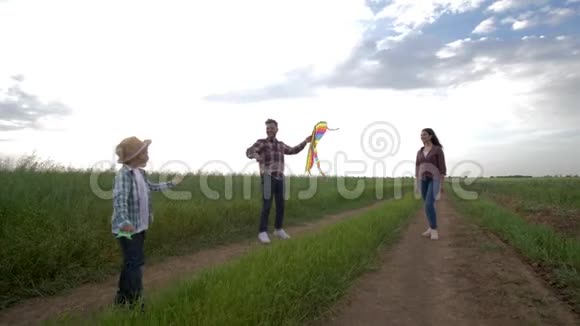 完美的家庭手里拿着风筝的孩子在阳光明媚的天空下在农村的年轻父母身边奔跑视频的预览图