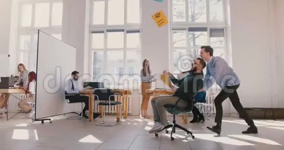 慢动作疯狂有趣的商人骑着办公椅沿着大办公室每个人都庆祝在空中扔纸视频的预览图