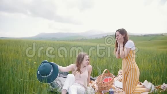 两个年轻有魅力的女人在草地上野餐其中一个把帽子扔到天空中视频的预览图