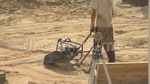 一名男工人在铺设瓷砖的道路施工过程中夯实沙子土壤凝结设备建筑视频的预览图
