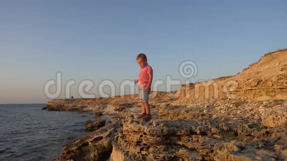 小男孩捡起一块石头扔进海里天空中的男孩海洋背景视频的预览图