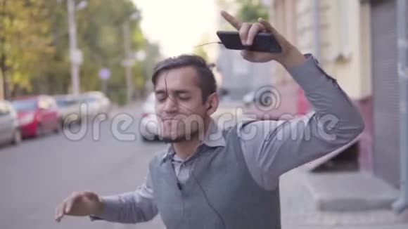 一个英俊的年轻人正在城里散步挥舞着手臂听耳机上的音乐慢动作视频的预览图