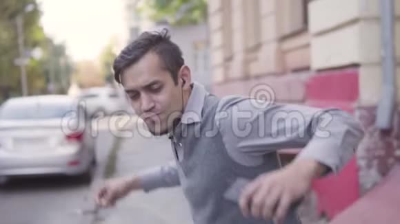 一个英俊的年轻人正在城里散步挥舞着手臂听耳机上的音乐慢动作视频的预览图