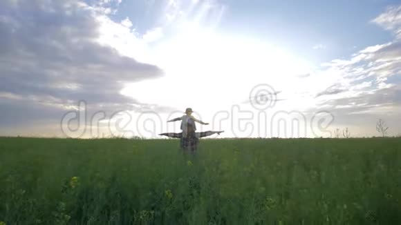 家庭游戏快乐的父亲在背景天空和日落的油菜地散步时把儿子扛在肩上视频的预览图