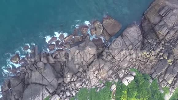 在海岸上挥舞着巨大的灰色石头和绿色灌木丛视频的预览图