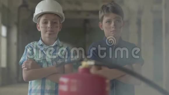 两个脸脏戴着防护头盔的小男孩看着灭火器火灾概念视频的预览图