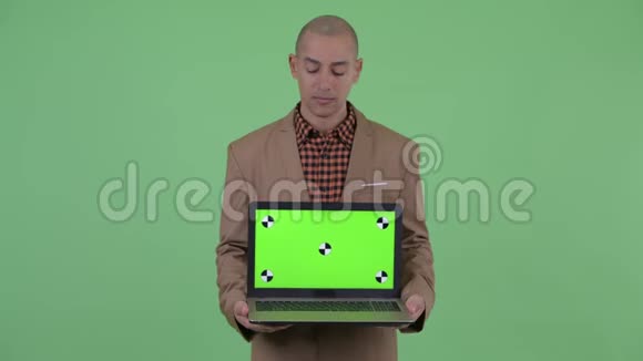 严肃的秃头多民族商人一边看着笔记本电脑一边抱怨视频的预览图