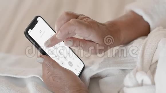 未被识别的穿着白色浴袍的成年女性在智能手机上拨打电话号码使用技术的概念视频的预览图