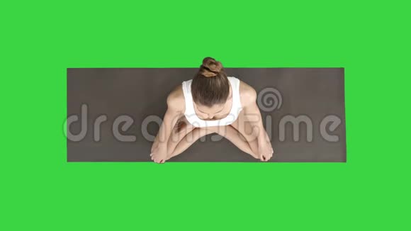 年轻的运动女性练习瑜伽坐在莲花姿势上在绿色的屏幕上深呼吸色度键视频的预览图