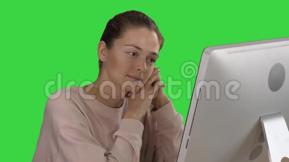 金发女孩带着粉红色的套头衫看着显示器上的电脑在绿色屏幕上观看视频色度键视频的预览图